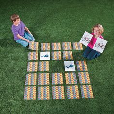 two children sitting on the grass with their paper cut out to look like an airplane