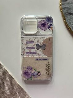 a cell phone case with flowers and butterflies on the back, sitting next to a feather