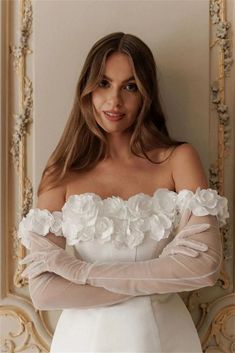 a woman in a white dress is posing with her arms crossed and flowers on the shoulder