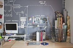 a desk with a computer, books and other items on it in front of a chalkboard wall