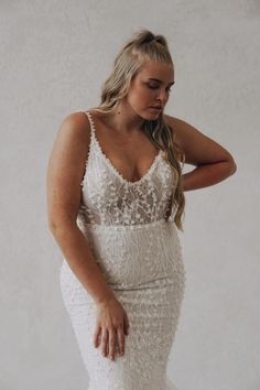 a woman in a white wedding dress with her hand on her hip and looking down