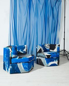 two blue chairs sitting next to each other in front of a curtain