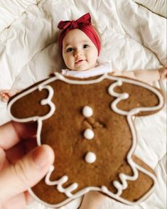 a baby in a red headband is holding up a cookie shaped like a ginger