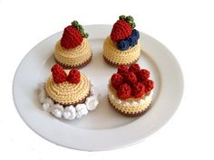 three crocheted cupcakes with strawberries on top sit on a plate