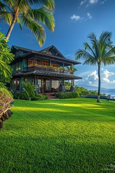 a large house sitting on top of a lush green field next to the ocean with palm trees