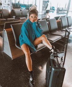 a woman sitting on top of a chair next to an airport baggage claim area with her luggage