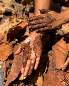 two hands with henna tattoos on them and leaves around the palms, all covered in brown