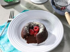 a chocolate bundt cake with powdered sugar and raspberries on top sits on a white plate