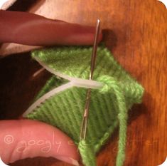 someone is crocheting the end of a green piece of yarn with a pair of scissors