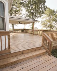 a wooden deck with steps leading up to the front door and covered porch area next to trees