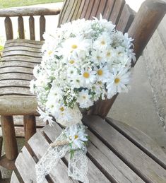 a bouquet of daisies sits on a wooden bench next to an old chair outside