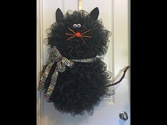 a black cat wreath hanging on a door with a bow around it's neck