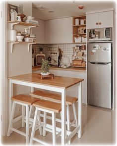 a kitchen with a table and stools next to a refrigerator in the middle of it