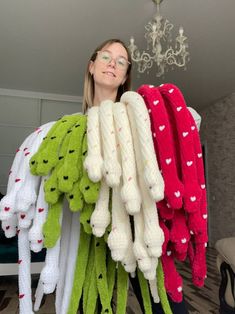 a woman standing next to a pile of knitted items in front of a chandelier