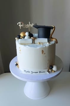 a white cake with gold decorations and a black hat on top is sitting on a table