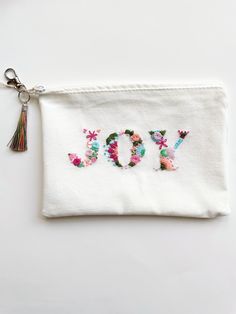 a white pouch with the word yo written in floral letters and tasseled keychain