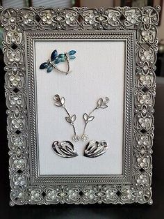 an ornate frame with two silver birds and pearls on the bottom, in front of a black table