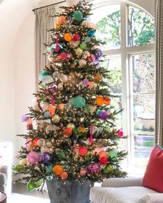 a brightly colored christmas tree in a living room with a large window and white chair