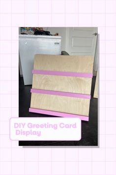 the diy greeting card display is made with plywood and pink tape on it