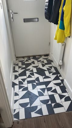 a white door with black and yellow tiles on the floor next to a coat rack