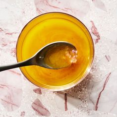 a spoon with some food in it on a marble table top next to an orange bowl