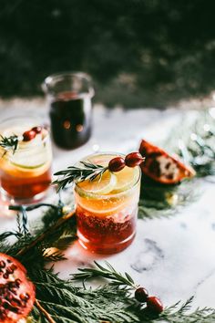 two glasses filled with drinks sitting on top of a table next to fruit and greenery