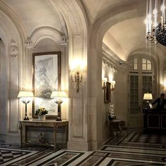 an elegant hallway with chandeliers and paintings on the walls