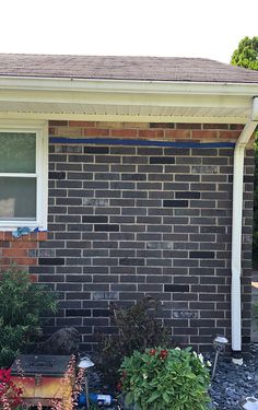 a brick house with flowers and plants in the front yard, next to a window