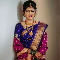 a woman in a purple and gold sari with jewelry on her head, standing against a wall