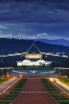 the building is lit up at night with lights shining on it's sides and trees in the foreground