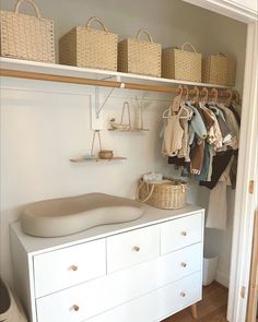 a white dresser sitting next to a closet filled with clothes and baskets on top of it