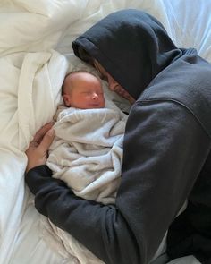 a man in a hoodie is holding a baby wrapped in a blanket on a bed