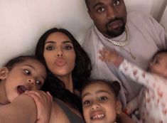 the family is posing for a selfie in their bed with one baby and two adults