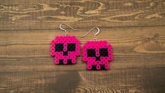 pink and black pixel earrings on wooden table with wood floor behind them, one piece has been cut out to make the shape of a skull