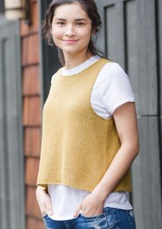 a woman standing in front of a brick building wearing a yellow sweater and blue jeans