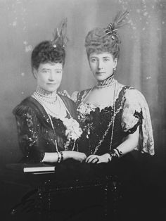 an old black and white photo of two women in formal dress, one wearing a feathered headdress