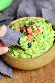 a person dipping guacamole into a wooden bowl with tortilla chips