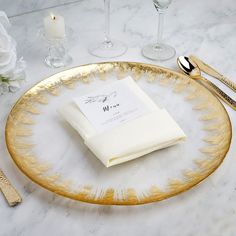 a gold plate with napkins and silverware sitting on a marble counter top next to wine glasses