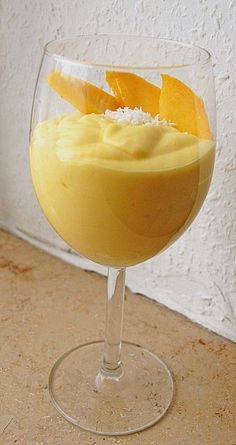 an orange dessert in a wine glass on a table with a white wall behind it