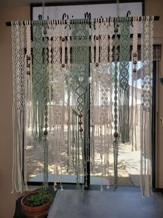 an open window with curtains and beads hanging from it's sides, next to a potted plant