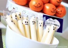 oranges with faces on them are in a white bowl next to halloween decorations and candy sticks