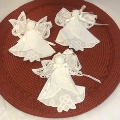 three little white angel decorations on a red place mat with lace and ribbon around the edges