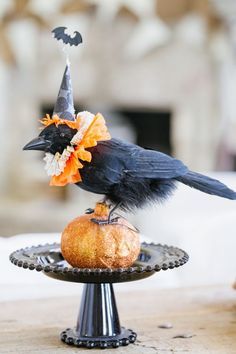 a black bird sitting on top of a metal cake plate with an orange and white flower