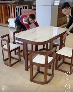 two men are looking at a table with chairs around it and one man is leaning over the table