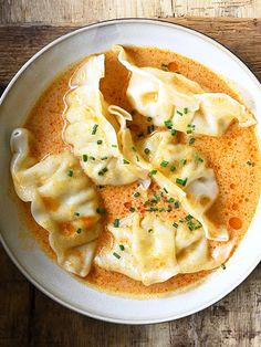 a white bowl filled with dumplings covered in sauce on top of a wooden table