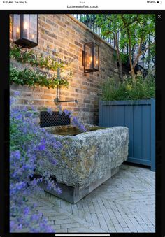 a stone fountain in front of a brick wall with plants growing on it and lights hanging from the ceiling