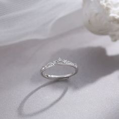 a white gold ring with three small diamonds on the side, sitting next to a flower