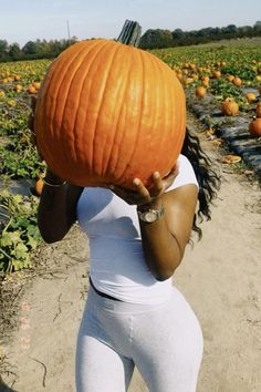 a woman holding a giant pumpkin over her face