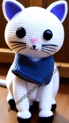 a crocheted white cat with black eyes and a blue scarf around its neck