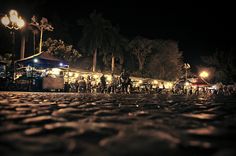 people are standing outside at night on the cobblestone street in front of tents